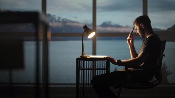 Serious Concentrated Young Male Student Studying at Home Office Sitting in Cozy Workplace at Night