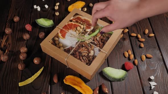 Closeup of a Woman Taking a Box of Various Nuts From a Wooden Table
