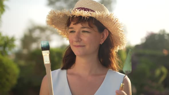 Thoughtful Beautiful Woman Holding Painting Brush and Knife Looking at Camera Smiling