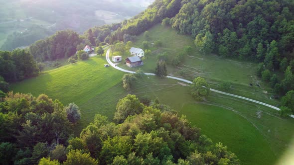 Aerial: Flying around an idyllic small farm on top of the hill surrounded with green meadows and for