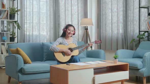 Woman Composer With Paper And Wearing Headphones And Smiling To Camera While Playing Guitar At Home