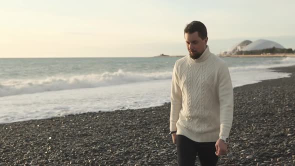 Adult Man in a Warm Sweater Strolls Along the Beach in the Autumn Time