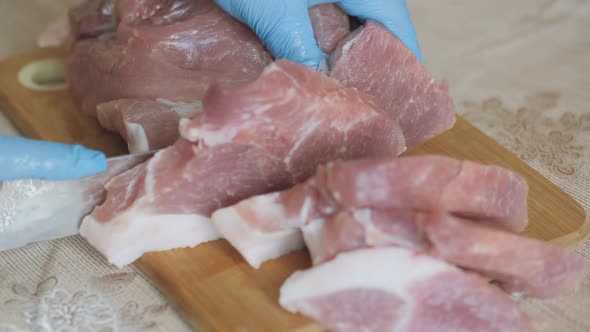 Cooking, Cutting Fresh Meat. Hands Dressed in Gloves and a Protective Disposable Blue Robe.