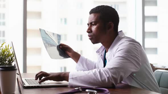 African American Black Male Doctor Is Analyzing MRI Brain Head Scan and Working on Laptop.