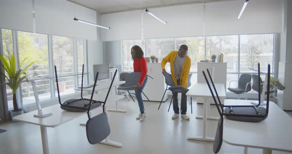 Young African Colleagues Putting Chairs Down in Office in Morning