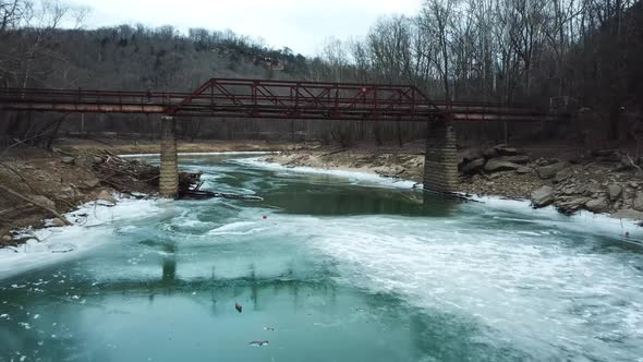 Drone Going Under Rusty Footbridge Over Icy River