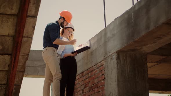 Two Architects Working On Building Model Blueprints. Engineers In Safety Helmet Construction House.