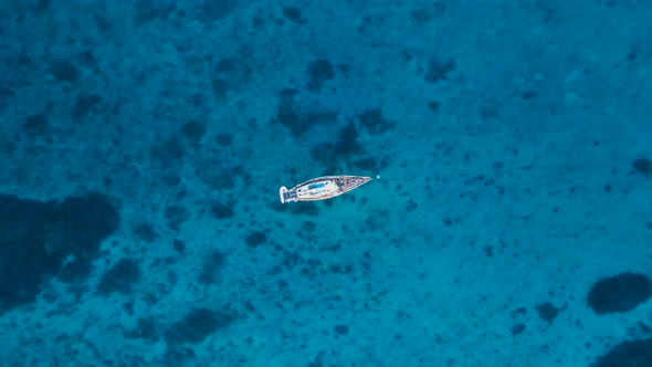 Yacht swaying and bobbing in the ocean revealing reef in the clear blue waters. High view looking do