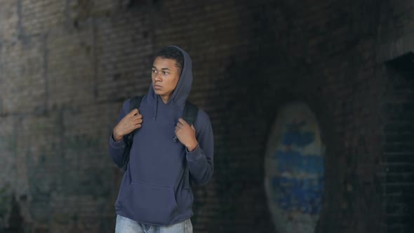 Thoughtful Black Teen in Hoodie With Backpack Walking Dangerous City Suburb