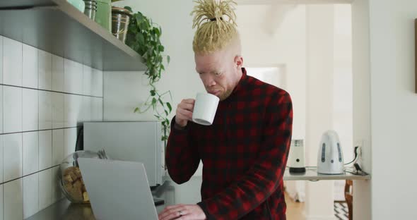 Thoughtful albino african american man with dreadlocks using laptop and drinking coffee