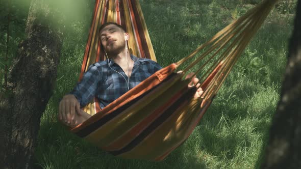 Male freelancer lying in hammock, relaxing and listening to music in earphones. Relax in hammock