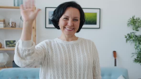 Slow Motion Portrait of Cheerful Woman Waving Hand and Smiling Standing Indoors at Home