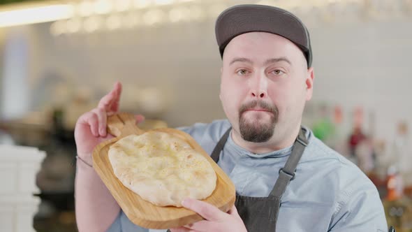Portrait of Positive Caucasian Plussize Man Looking at Camera Smelling Delicious Baked Pinza