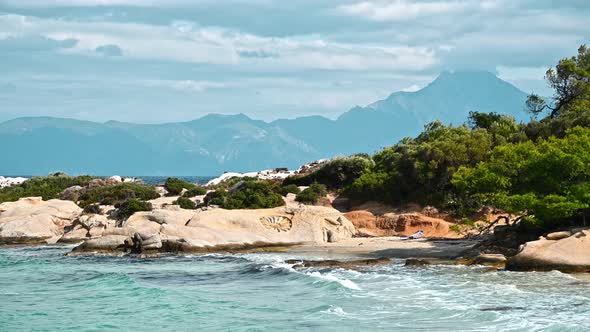 Aegean sea coast with greenery around, rocks, bushes and trees, blue water with waves, Greece