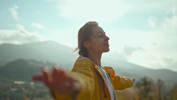 Young Woman Wearing a Yellow Jacket Raising Her Arms Into the Blue Sky and Enjoying the View Above