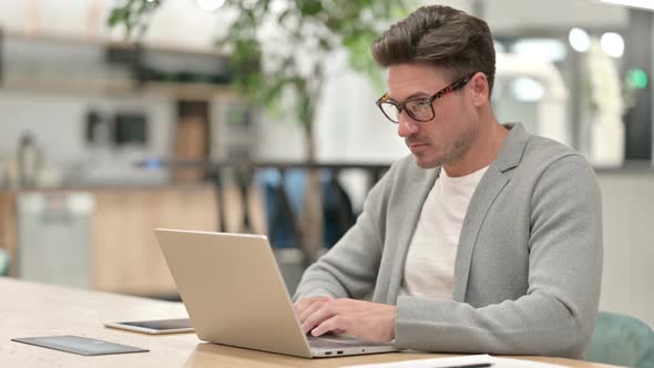 Serious Middle Aged Man Using Laptop in Office 