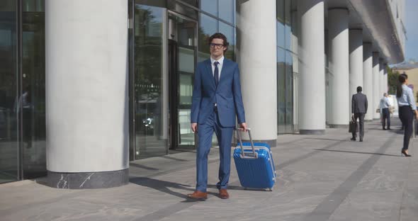 Young Stylish Businessman Walking with Suitcase Near Airport Building