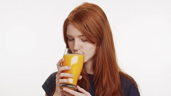 Young Smiling Cute Foxy Girl Wearing Dark Blue Shirt Drinking Orange Juice From Glass on White