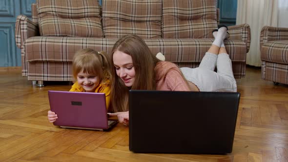 Mother and Small Daughter Child Sit on Warm Wooden Floor at Home Working on Laptop Watching Cartoon