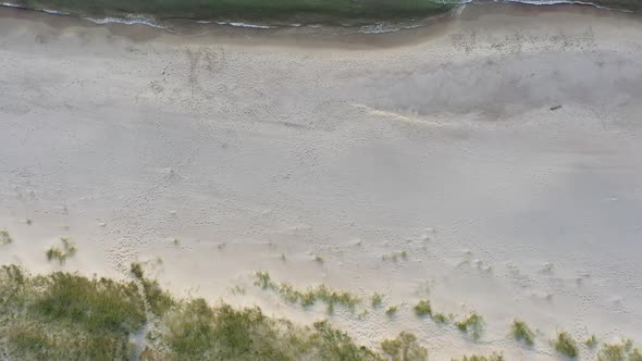 AERIAL: Top View Ascending Shot of Deserted Sandy Beach on a Lovely Evening with visible Seashore