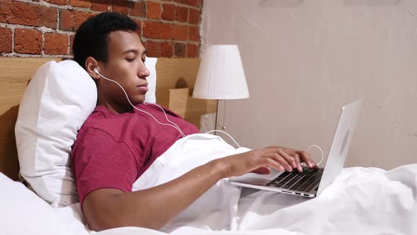 Video Chat for Work By Young African Man Lying in Bed at Night