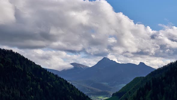 In summer, clouds spill over mountain peaks in a wooded basin