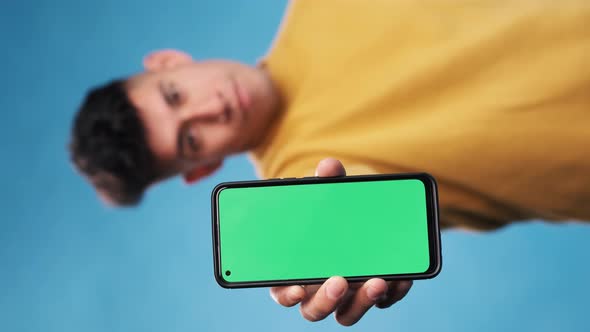 Man showing a smartphone with green screen while standing over an blue background. Slow motion