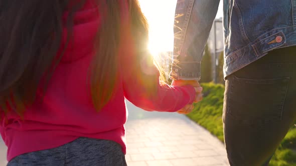 Dad and Daughter Walk Around Their Area at Sunset. Child Holds Father's Hand. Slow Motion