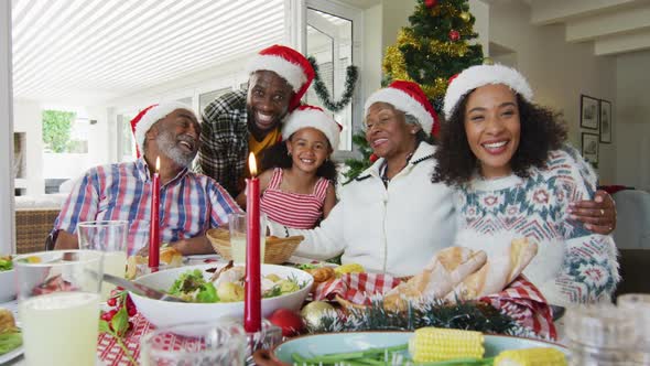 Happy african american multi generation family wearing santa hats, taking holiday photo