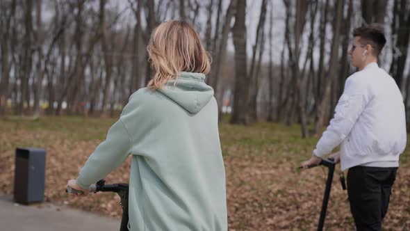 A Beautiful Couple of Young People Ride in the Park on Electric Scooters