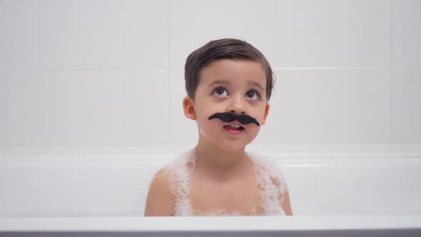 Small Boy with a Black Mustache Sits in the Bathroom