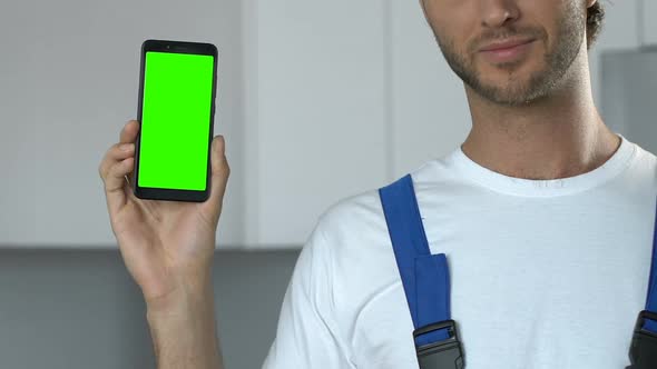 Attractive repairman demonstrating greenscreen smartphone to camera