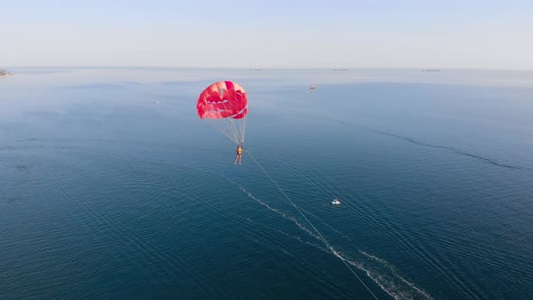 Towing Red Parachute Behind a Jetski Over the Sea Along the Beach at Sunset
