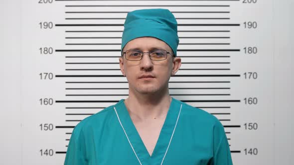 Mugshot of a Surgeon in Glasses, in Green Clothes, at the Police Station