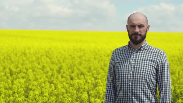 Young Bearded Farmer on Rapeseed Blooming Plants