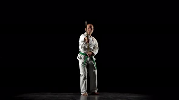 Kendo Fighter on White Kimono Practicing Martial Art with the Bamboo Bokken on Black Background.