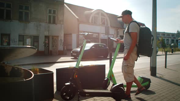 Man Uses an App on His Smartphone to Unlock Electric Scooter Outside