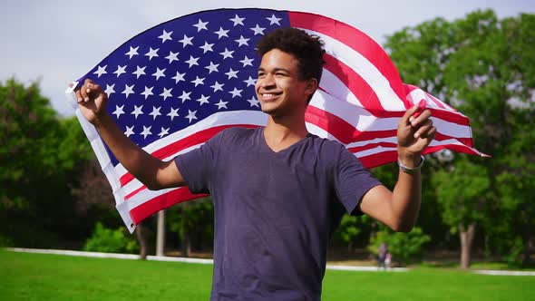 Attractive African American Man Holding American Flag in His Hands on the Back Walking in the Green