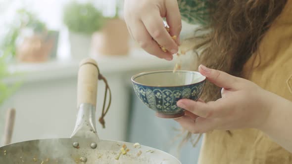 Woman adding peanut to frying pan with wok