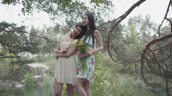 Portrait Two Cute Young Women in Short Summer Dresses Standing on Rocky Ground with Wild Flowers