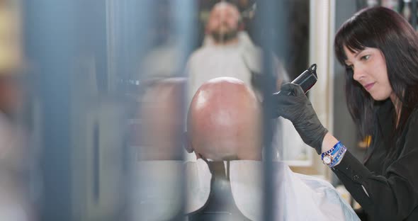 First Plan in Slightly Blurred Young Bearded Man with Clean Shaved Head is Sitting on the Barber's