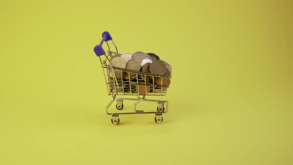 Shopping Cart with Coins, Banknotes and Credit Cards Drive on a Yellow Background