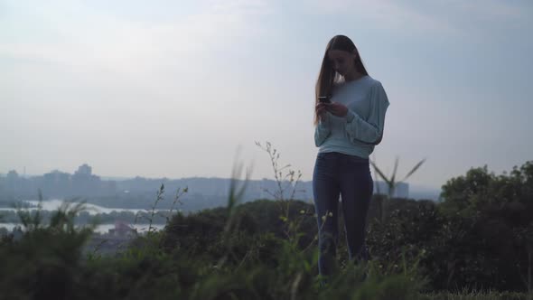 A Young Girl Stands on a Hill and Looking at Your Phone.