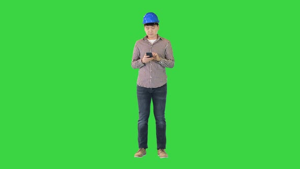 Smart Asian Engineer Holding Smartphone and Using It on a Green Screen Chroma Key alt