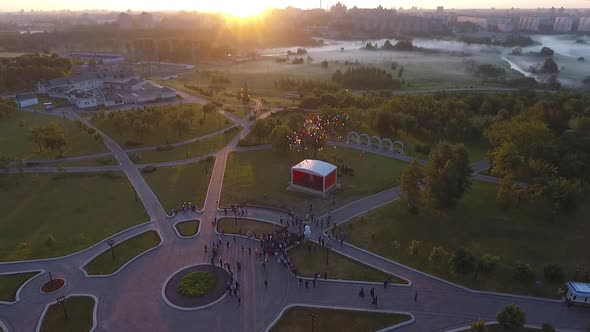 Students Launch Colourful Balloons in Sunrise Lights in the City Park Aerial alt