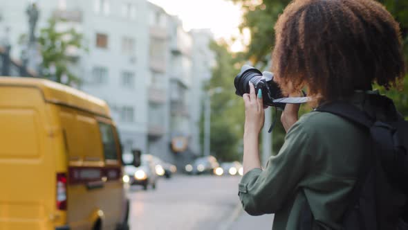 Young African Woman Tourist with Curly Hair and Backpack Travelling Photographing Attractions Using