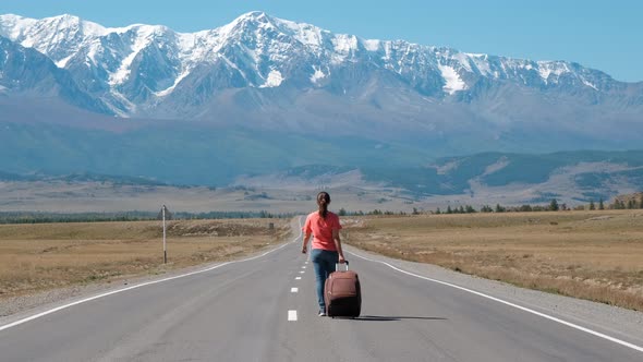 Woman with Suitcase Walking Along Mountain Road