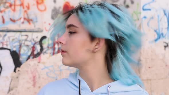 Blue haired teenage girl in hoodie turning left. Head portrait against graffiti