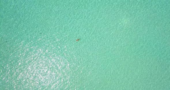 Aerial drone view of a woman floating and swimming on a tropical island.