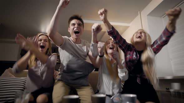 Sport Fans Boys and Girls Sitting on Couch in Living Room and Watching Sport Match